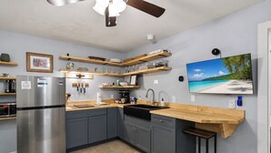 A modern kitchen with grey cabinets, a stainless steel refrigerator, wooden countertops, and a built-in island with a sink. - Brick House By the Bay | Bay Walk + Local Life (Shalimar)