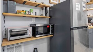 A kitchen with a microwave, toaster, and refrigerator. Shelves hold spices and a coffee maker. - Brick House By the Bay | Bay Walk + Local Life (Shalimar)