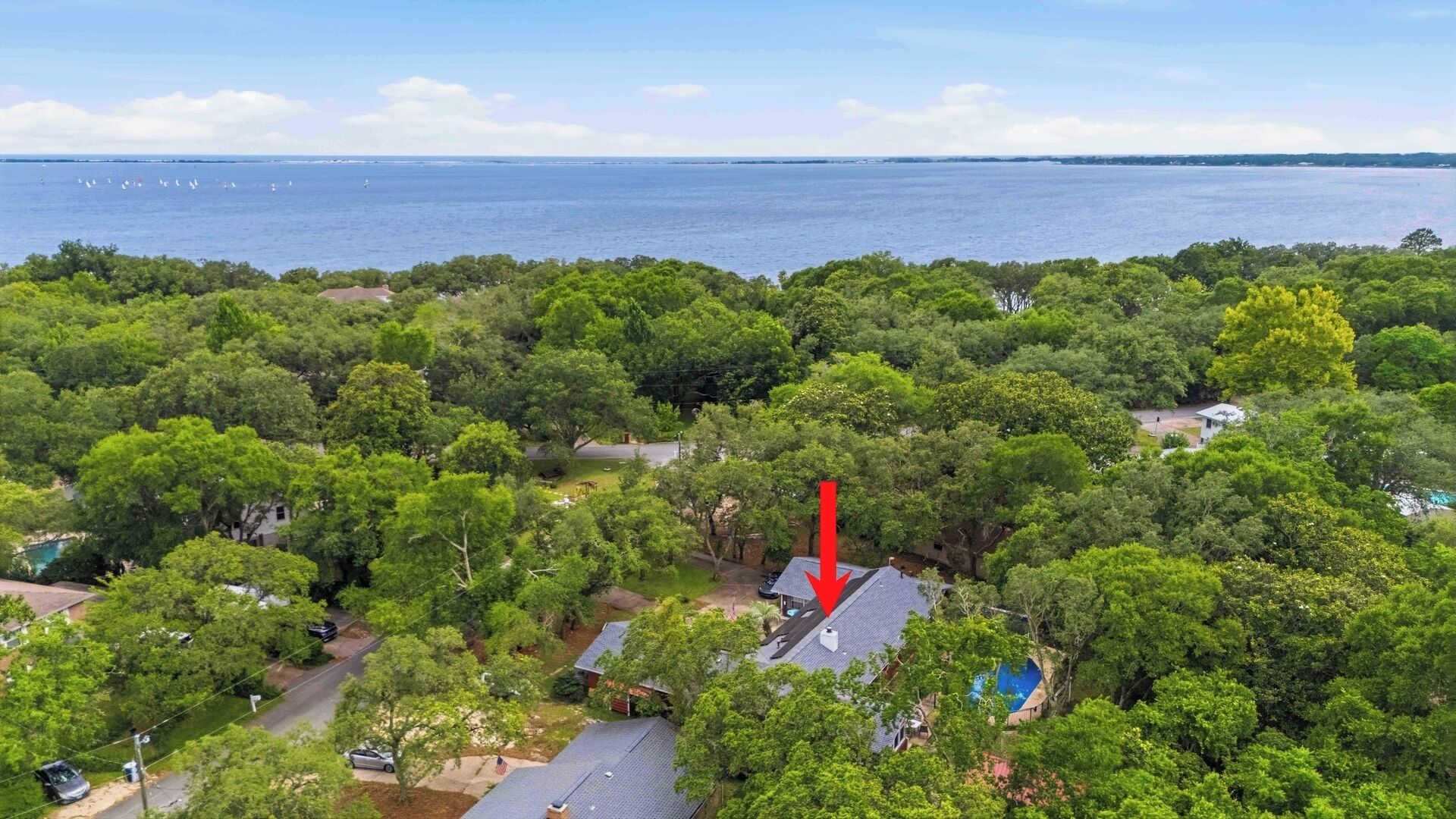 Vista aérea de una zona residencial con abundante vegetación, una piscina y vistas al mar.