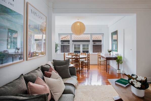 A modern living room with a sofa, dining table, and chairs, a hanging light fixture, and framed artwork on the walls.