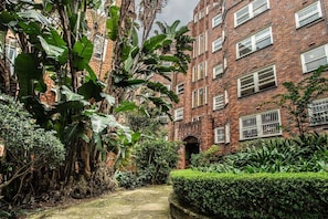 A brick building with multiple windows, a central entrance, and lush greenery surrounding the structure. - Winchester Stylish Art Deco Apartment in Edgecliff (Edgecliff)