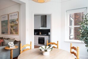 Eine moderne Küche mit weißen Schränken, einer schwarzen Arbeitsplatte und Edelstahlgeräten. Es gibt eine Essecke mit einem runden Tisch und Holzstühlen.