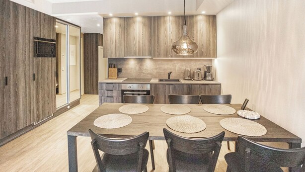 A modern kitchen with wooden cabinets, a dining table with placemats, and a hanging pendant light. - Äkäspokka by Interhome (Äkäslompolo)