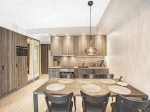 A modern kitchen with wooden cabinets, a dining table with placemats, and a hanging pendant light. - Äkäspokka by Interhome (Äkäslompolo)