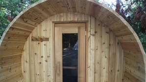 Une cabane en bois avec un toit circulaire, une porte centrale et un banc sur le côté gauche.