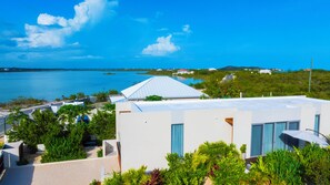 A modern building with a flat roof, surrounded by lush greenery and overlooking a calm body of water.