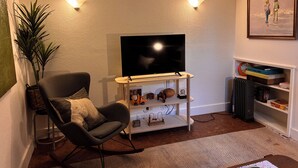 A living room with a flat-screen TV on a stand, a rocking chair, a bookshelf, and a framed picture on the wall. - Cool apartment in vibrant Seattle neighborhood.Restaurants, bars and Light Rail. (Seattle)