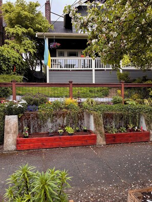 A residential property with a raised garden bed, a white fence, and a house with a dark roof. - Cool apartment in vibrant Seattle neighborhood.Restaurants, bars and Light Rail. (Seattle)