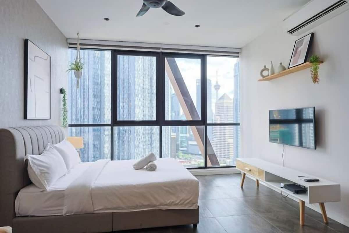 Ein modernes Schlafzimmer mit einem großen Bett, einem Fernseher, einer Bank und Blick auf die Stadt.