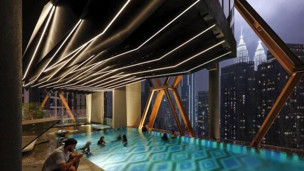 Piscina infinita no terraço com vista para a cidade, arquitetura moderna e uma pessoa usando um smartphone.