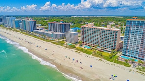 A beachfront hotel with multiple high-rise buildings, a sandy beach, and a clear sky. - 1416 Sandcastle South-Surfs Up (Myrtle Beach)