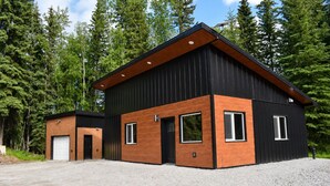 Moderni kaksikerroksinen rakennus, jonka ulkoseinät ovat mustat ja jossa on puuelementtejä, ja jonka ympärillä on metsä.