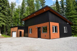 Ein modernes, zweistöckiges Gebäude mit schwarzer Fassade und Holzakzenten, umgeben von einem Wald.