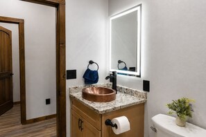 Ein Badezimmer mit einem Kupferwaschbecken, einem Spiegel, einem Handtuchhalter und einer Toilette.