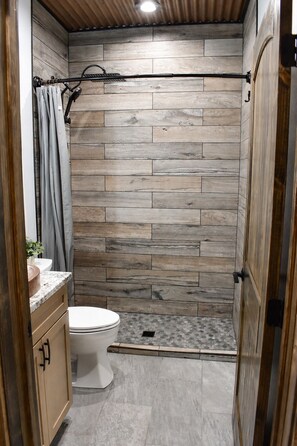 Ein Badezimmer mit Holzwand, Dusche, Toilette und Waschbecken mit Marmorplatte.