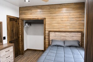 Ein Schlafzimmer mit hölzernem Kopfteil, einem Bett mit grauer Bettwäsche, einem Holzschrank und einer weißen Wand.