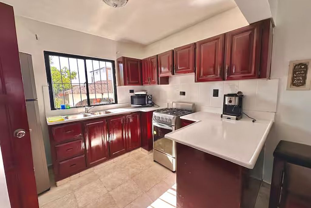 A kitchen with red cabinets, a white countertop, a stove, a microwave, and a refrigerator.