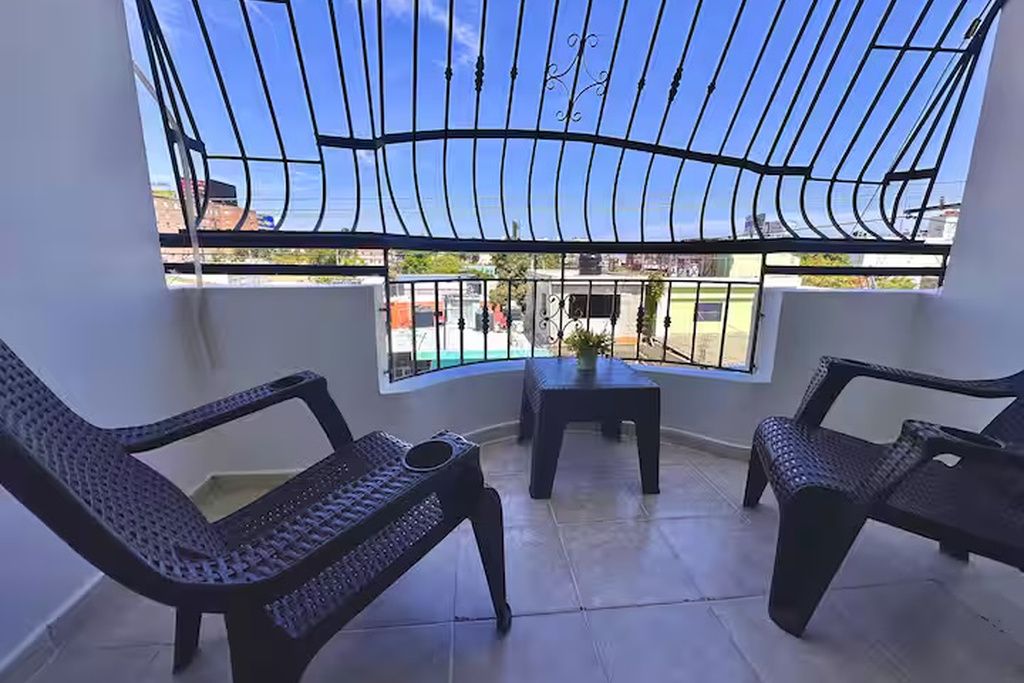 A room with two chairs, a small table, and a view through a window with a metal grill.