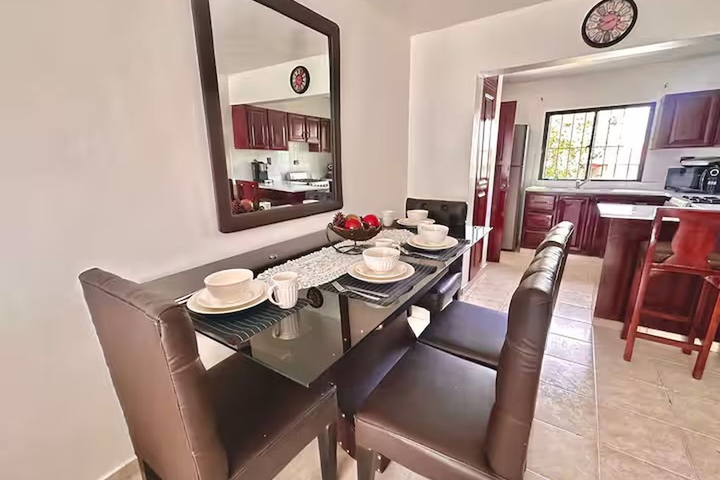 Un área de comedor con una mesa de vidrio, sillas de cuero marrón y un espejo grande sobre ella.