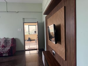 Une pièce avec un mur recouvert de lambris en bois, un téléviseur fixé sur ce mur, un canapé rouge et une porte donnant sur un balcon.