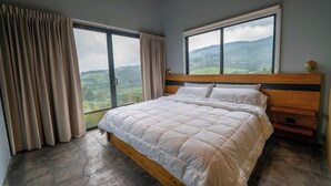 Un dormitorio con una cama grande, cabecera de madera y dos ventanas que dan a un paisaje montañoso.