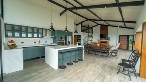 A modern kitchen with a central island, bar stools, and a dining area with a staircase.