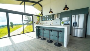 A modern kitchen with a large island, bar stools, stainless steel appliances, and a view of a green landscape.