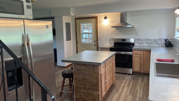Una cocina moderna con electrodomésticos de acero inoxidable, armarios de madera, una isla central y una escalera.