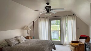 Un dormitorio con cama, una silla, ventilador de techo, lámpara y vistas por una puerta.