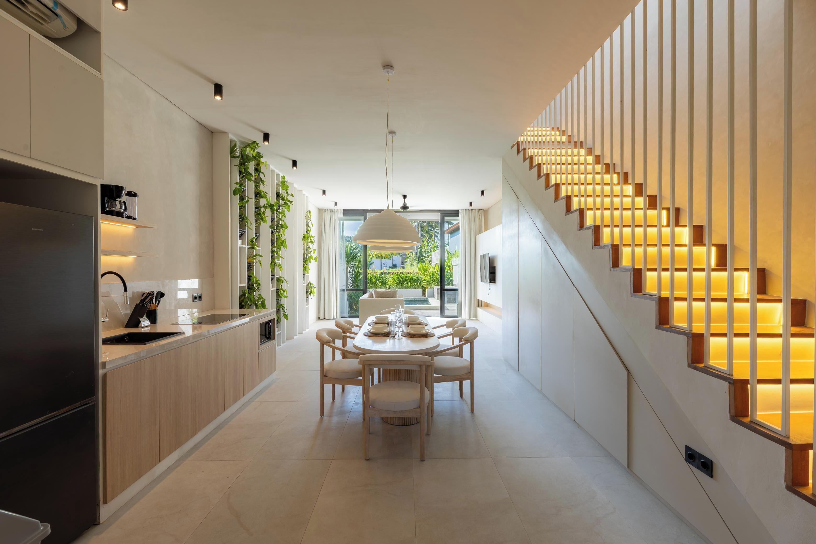 Una cocina moderna con comedor, una escalera con escalones iluminados y vista a zonas verdes.