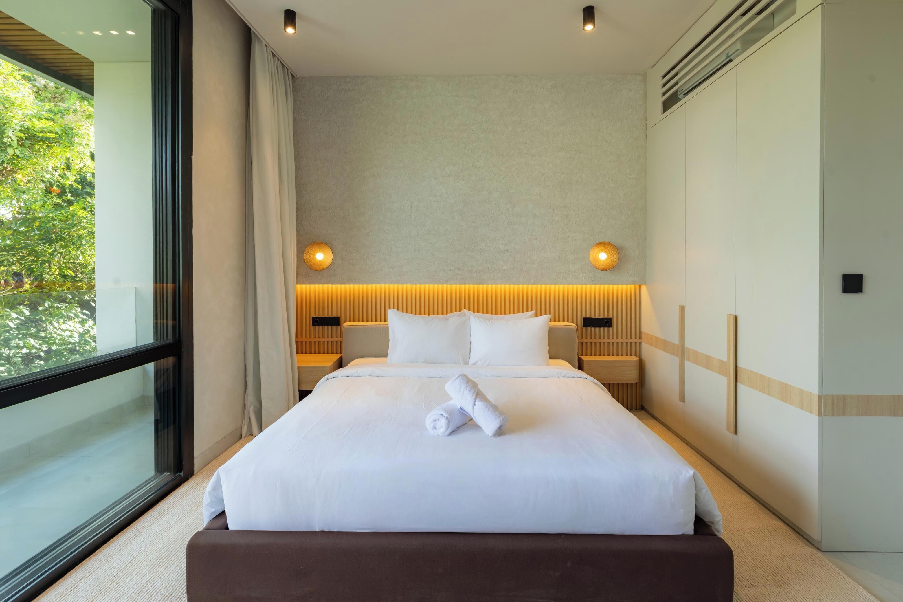 Una habitación de hotel moderna con una cama grande, dos mesitas de noche, un ventanal y vistas a zonas verdes.
