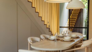 A modern dining area with a long table, white chairs, and a unique vertical light fixture. - Serenity Ubud by Betterplace (Ubud)