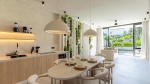 A modern kitchen with a central island, pendant lights, and a view of a lush garden through large windows. - Serenity Ubud by Betterplace (Ubud)