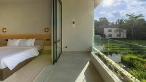 A modern bedroom with a large bed, a glass door leading to a balcony with a view of a garden and a distant building. - Serenity Ubud by Betterplace (Ubud)