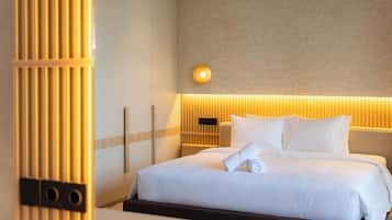 A hotel room with a bed, a nightstand, a wall-mounted light, and a vertical wooden panel.