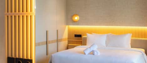 A hotel room with a bed, a nightstand, a wall-mounted light, and a vertical wooden panel.