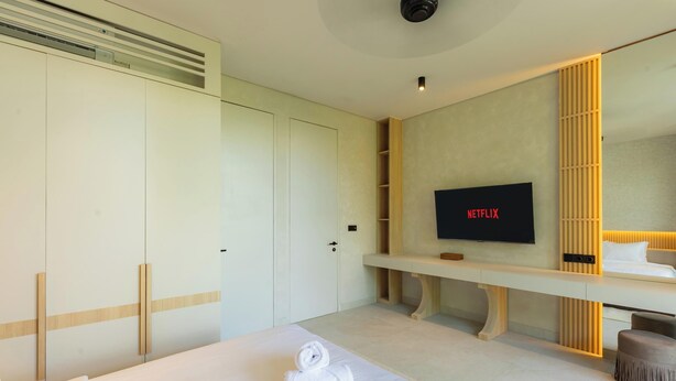 A modern hotel room with a large bed, a TV mounted on the wall, and a wooden vanity. - Serenity Ubud by Betterplace (Ubud)