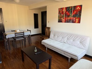 Ein Wohnzimmer mit weißem Sofa, einem Esstisch mit Stühlen, einem kleinen Couchtisch und einem Bild an der Wand.