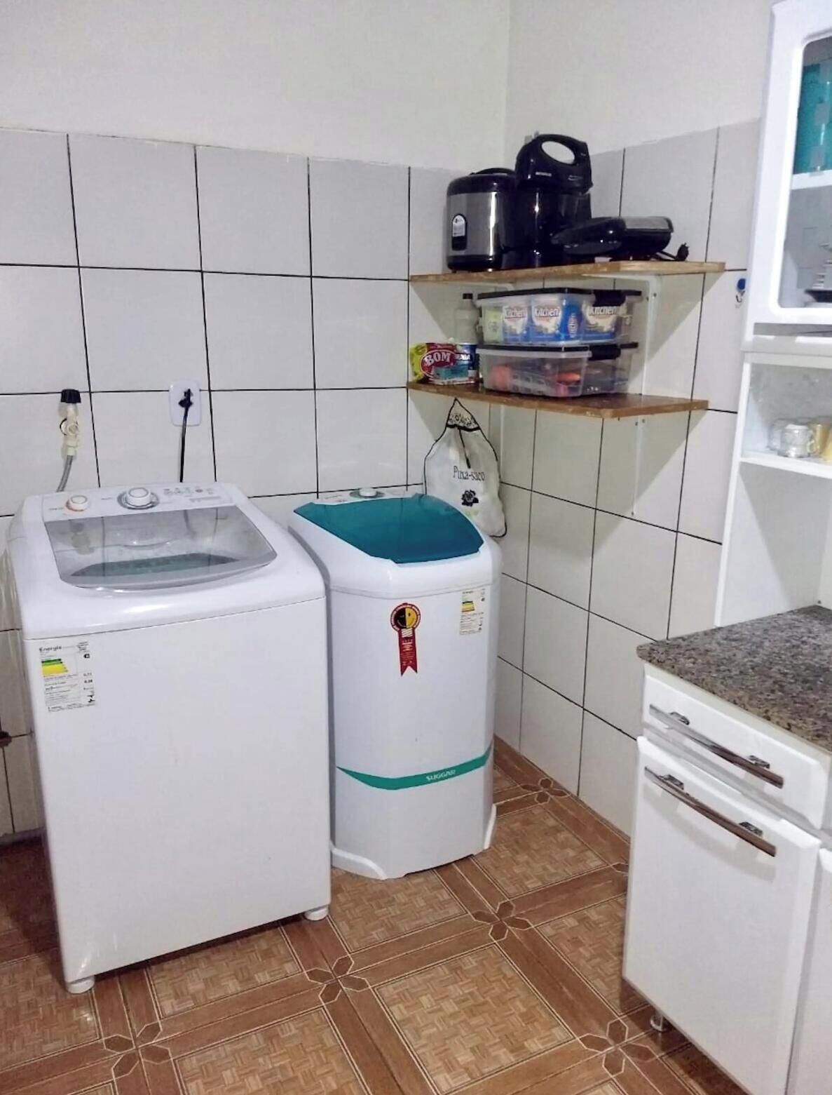 Een kleine keuken met een wasmachine, een compacte koelkast en een plank met diverse spullen.