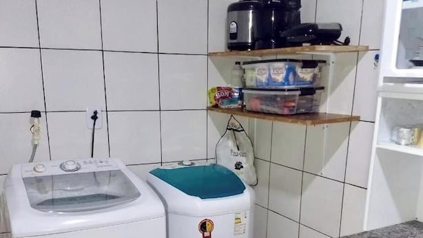 Uma cozinha compacta com máquina de lavar, frigorífico pequeno e uma estante com diversos objetos.