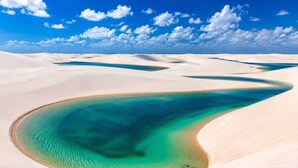 Paisagem desértica com dunas de areia e uma extensão de água azul-turquesa.