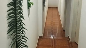 Um corredor com piso de azulejos, uma planta em vaso e um ponto de luz fixado na parede.