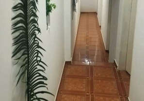 A hallway with a tiled floor, a potted plant, and a wall-mounted light fixture. - Barreirinhas House, near...  Lençois Maranhenses, come with a group of up to 14 people. (Barreirinhas)