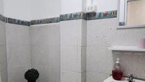 Un baño con inodoro, lavamanos, cubo de basura y una pequeña planta en maceta.