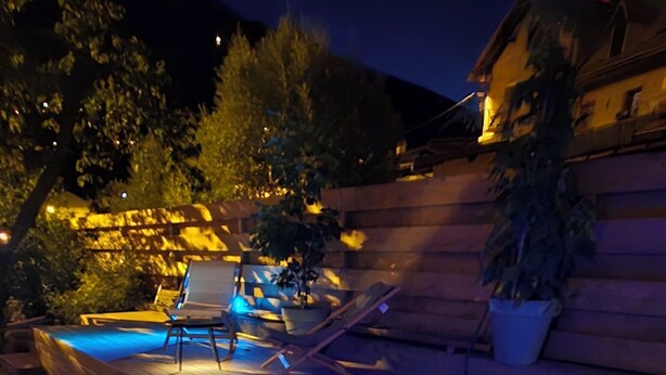 A hot tub with blue lighting, surrounded by a wooden deck and a pool.