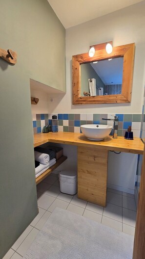 Une salle de bain avec un meuble-lavabo en bois, un lavabo blanc, un miroir avec éclairage intégré et un mur recouvert de carreaux.