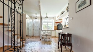 A spacious hallway with a tiled floor, a staircase with a wrought iron railing, a dining area with chairs, and a table with a lamp. - Stągiewna Old Town Apartment (Gdańsk)