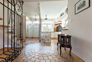A spacious hallway with a tiled floor, a staircase with a wrought iron railing, a dining area with chairs, and a table with a lamp. - Stągiewna Old Town Apartment (Gdańsk)