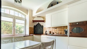 A kitchen with white cabinetry, a dining table, chairs, a window with blinds, and a vintage oven. - Stągiewna Old Town Apartment (Gdańsk)