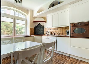 A kitchen with white cabinetry, a dining table, chairs, a window with blinds, and a vintage oven. - Stągiewna Old Town Apartment (Gdańsk)